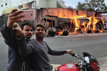 Two men stop to take a selfie next to a truck from neighbouring Tamil Nadu after it was set ablaze by a mob in Bengaluru